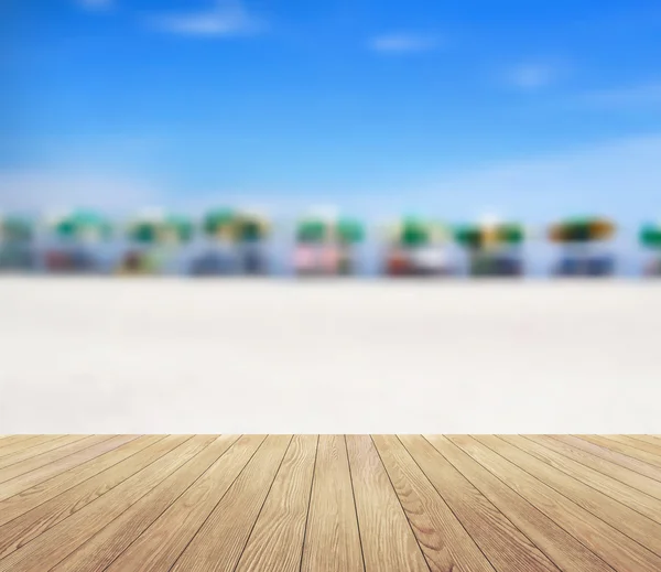 Houten planken vloer met stoelen en parasol op tropisch strand wazig achtergrond — Stockvector