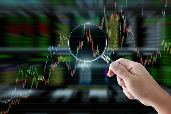 Hand holding magnifying glass with stock market graph background — 图库照片