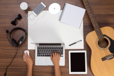 Bir dizüstü bilgisayar akustik gitar ve kulaklık kullanarak office Resepsiyon arka plan ele