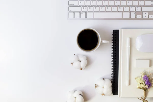 Minimal Office desk table with Keyboard computer, coffee cup, mouse, white pen, cotton flowers, eraser on a white table with copy space for input your text, White color workplace composition, flat lay, top view