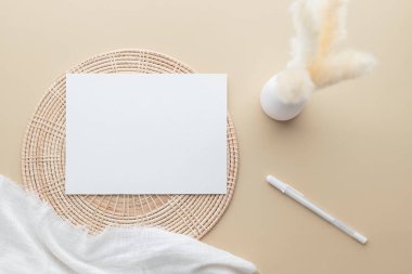Beyaz davetiye kartı, bej arkaplanda boş kağıt maketi vazoda sazlık, beyaz battaniye, Rattan sepeti, düz yatak, üst görünüm, boşluk kopyalama