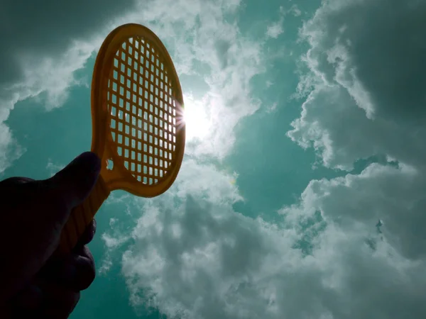 badminton racket holding on hand towards sun light on sky background.
