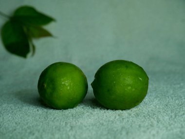 Beyaz kumaşta bulanık yaprak arkaplanı olan çift yeşil limon.
