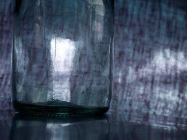 Gri zemin üzerinde parlak ışık yansıması olan şeffaf cam şişe.