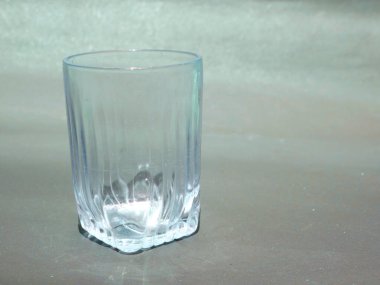 Gri arkaplanda gün ışığında izole edilmiş su bardağı, mutfak çatal bıçak ürünü görüntüsü.