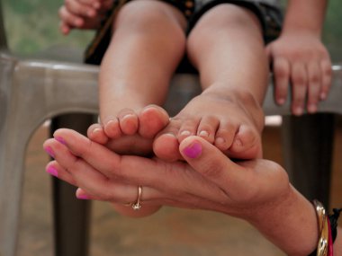 Küçük çocuk ayakları kadın eli üzerinde, erkek ayağı ile sunulan şefkatli konsept.