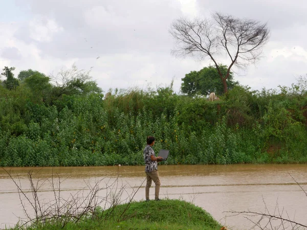 Asian male holding laptop around river bank amazing natural lifestyle view.