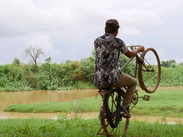Indian boy stunting with old bicycle at green grass field on river bank background.