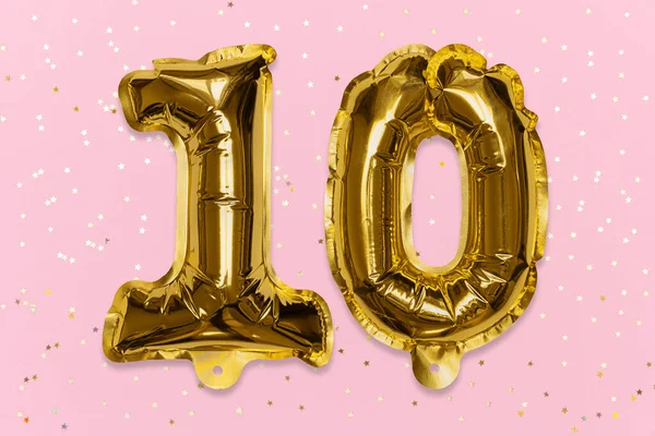 The number of the balloon made of golden foil, the number ten on a pink background with sequins.