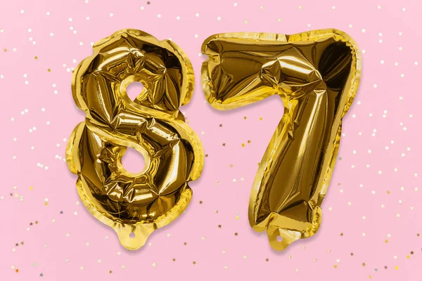 The number of the balloon made of golden foil, the number eighty-seven on a pink background with sequins. Birthday greeting card with inscription 87. Numerical digit, Celebration event, template.