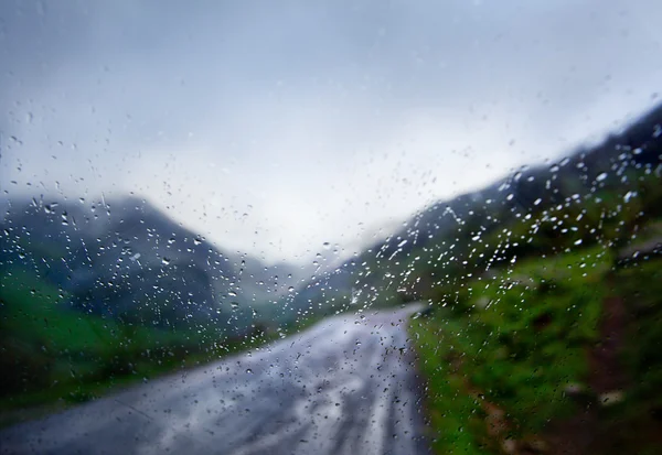 Des gouttes de pluie tombent par la fenêtre de la voiture sur la route. Image abstraite — Photo