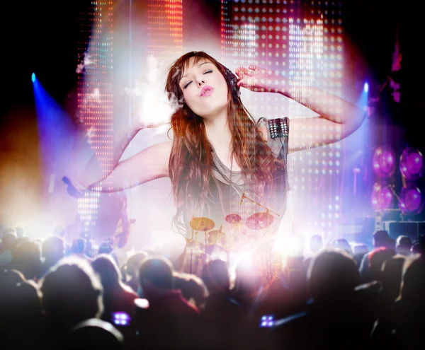 Beautiful woman listening to music with headphones and silhouettes of concert crowd in front of bright stage lights.