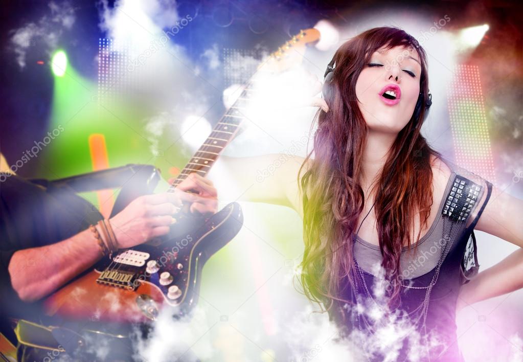 Beautiful woman listening to music with headphones. Live music background with guitar and bright lights on stage.