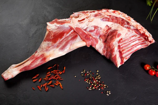 Vers en ruwe vlees. Been van lamb ongekookt tomaat en peper op zwarte achtergrond — Stockfoto