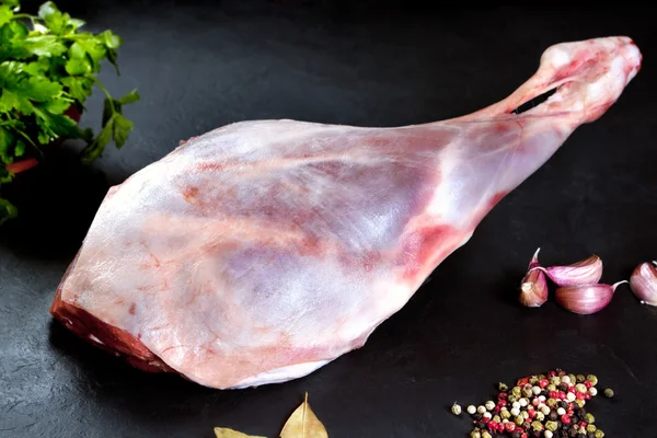 Frisches und rohes Fleisch. Lammkeule mit ungekochten Tomaten und Paprika auf schwarzem Hintergrund — Stockfoto