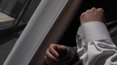 İş adamı gömlek kollarının düğmelerini ilikliyor, yakın plan. Beyaz gömlekli başarılı bir adam kollarına düğme takar, yakın plan, erkek eli beyaz gömleği ilikler.