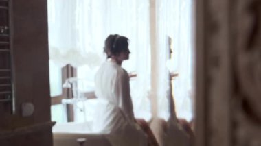 Beyaz cüppeli bir kız küvetin kenarında oturur ve pencereden dışarı bakar.