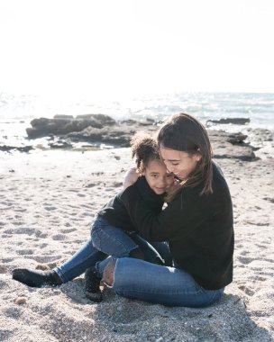 Anne sahilde kızını sevgiyle kucaklıyor.