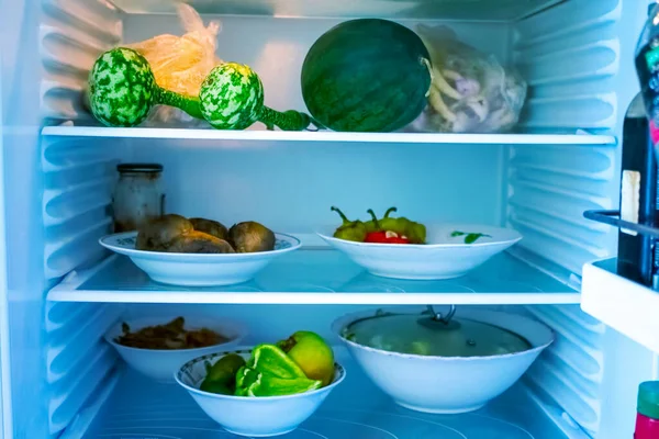 Shelves of an open frige refrigerator with different food, cooked food in pot and plastic container.