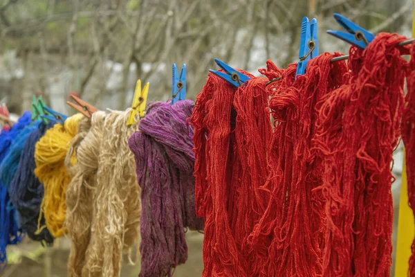 Woolen colorful threads are hanging on a clothesline with clothespins outdoor