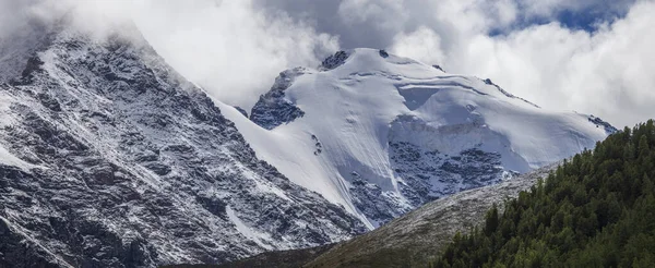 Snow-capped mountain peaks in the clouds, panoramic view. Glaciers, rocks and fresh snow.