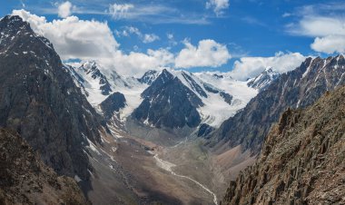 Gün ışığında dağ manzarası, derin vadi. Karla kaplı zirveler ve bulutlu mavi gökyüzü.