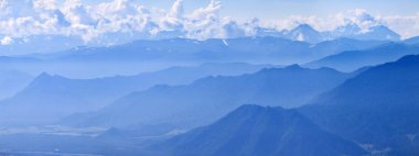 Mavi sisli dağlar, panoramik manzara. Bulutlardaki, vadideki ve dağlardaki tepeler.