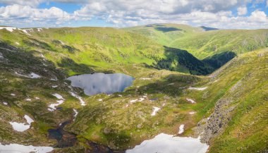 Dağlarda ilkbahar. Yamaçlarda kar, yeşil çayırlar, göl..