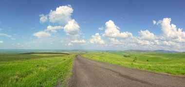 Yeşil tarlalar, uzak dağlar ve mavi bulutlu gökyüzü arasındaki yolun panoramik görüntüsü