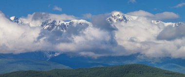 Bulutlarda karla kaplı dağ zirveleri. Dağlarda gezmek, tırmanmak. Panoramik görünüm.