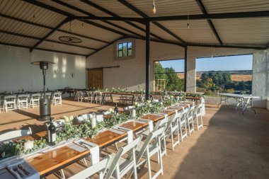 Düğün resepsiyonu, çiftlik ambarındaki misafirler için yemek masası hazırlıyor. Kırsal manzarası için uzun cam pencereli bir kutlama etkinliği..