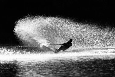 Su kayağı yapan tanınmayan genç sporcu slalom kayağı yaparken dramatik bir zıtlık fotoğrafı için dikey su uyandırma spreyini klasik sepia siyah beyaz tonda oyuyor..