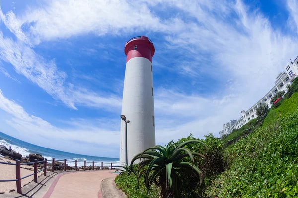 Deniz feneri boyunca kayalık sahil şeridi boyunca kırmızı ve beyaz boyalı apartmanlar ve yazlık mavi gökyüzü..