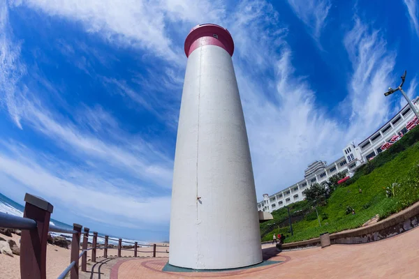 Deniz feneri boyunca kayalık sahil şeridi boyunca kırmızı ve beyaz boyalı apartmanlar ve yazlık mavi gökyüzü..