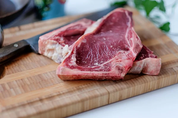 Stücke von rohem Rindfleisch auf dem Schneidbrett mit etwas grünem Salat in t — Stockfoto