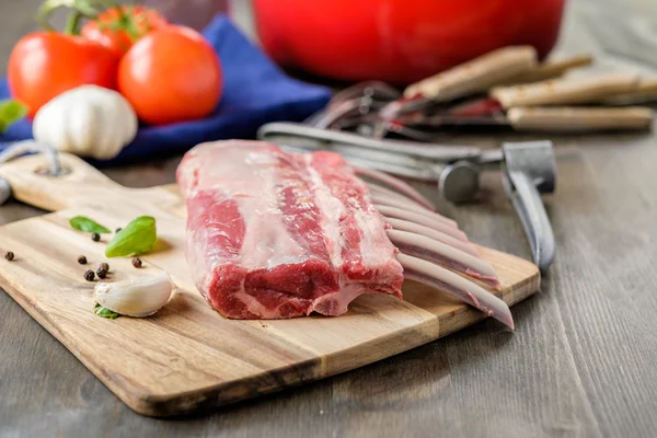 Rohe Lammstange mit etwas Tomaten und Kräutern im Hintergrund — Stockfoto