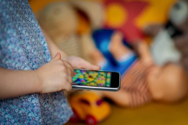 Küçük bir çocuk telefonda oynuyor ve çocukların oyuncakları arkada yatıyor. Seçici Odaklanma