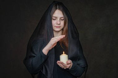 Siyahlar giymiş bir kız önünde yanan bir mum tutuyor ve elini üzerine koyuyor. Seçici Odaklanma