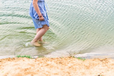 Bir kız kıyıya yakın sığ sularda yürür, sadece vücudunun alt kısmı görünür.
