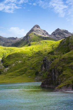 Alplerin ortasındaki dağ gölü. Mavi göllü yeşil dağda bir yaz. Alp dağları, ışık ve bulutların gölgesi..