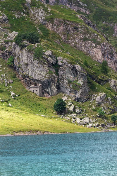Alplerin ortasındaki dağ gölü. Yeşil dağda, mavi gölü ve küçük bir evi olan bir yaz. Alp dağları, ışık ve bulutların gölgesi..