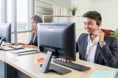 Çağrı merkezinde gülümseyen genç işadamı meslektaşlarıyla birlikte kulaklıkla masanın başında oturuyor.