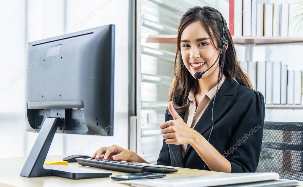 Smiling friendly asian female call-center agent with headset showing thumbs up for working on support hotline in the office, Service mind concept