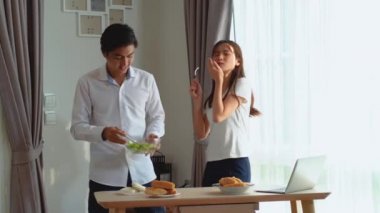 Genç ve mutlu Asyalı çift birlikte dans ediyor. Birlikte gülüyor, evde yemek hazırlıyor, kaygısız, neşeli karı ve koca sağlıklı romantik yemek pişiriyor. Modern mutfakta müzik dinliyor.
