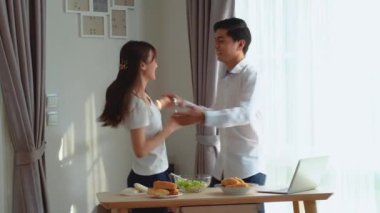 Genç ve mutlu Asyalı çift birlikte dans ediyor. Birlikte gülüyor, evde yemek hazırlıyor, kaygısız, neşeli karı ve koca sağlıklı romantik yemek pişiriyor. Modern mutfakta müzik dinliyor.