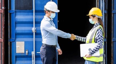 Businessman and engineer woman shake hands as hello in the container cargo harbor to loading containers. Shaking hands after the inspection or investigation are complete. Industrial and business concept