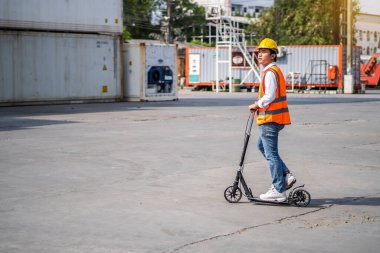 Young engineer or supervisor riding a e-scooter checking and control loading Containers box from Cargo at harbor, Transportation and logistic concept