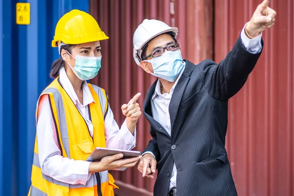 Industrial worker woman and engineer control worker using tablet device and meeting in front of container and cargo. Business people with confident and smart working in shipping transport industry