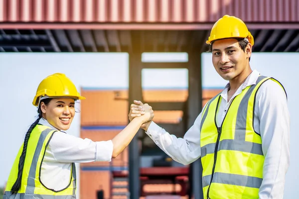 Engineer asian men and women shake hand together in front of cargo container with concept of successful in shipping workplace