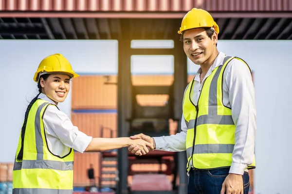 Engineer asian men and women shake hand together in front of cargo container with concept of successful in shipping workplace